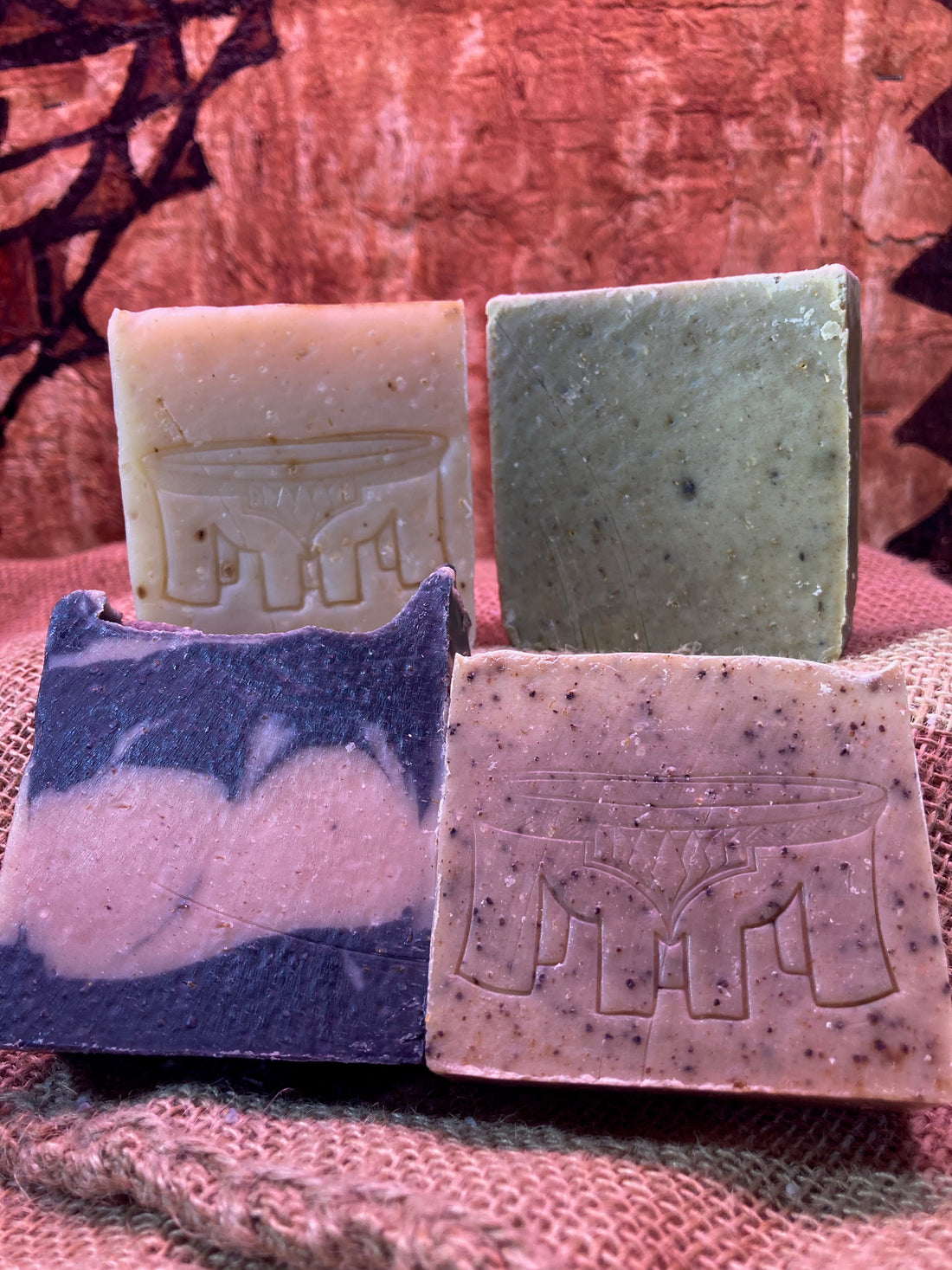 Four bars of soap on a burlap bag with a tapa cloth tapestry in the background