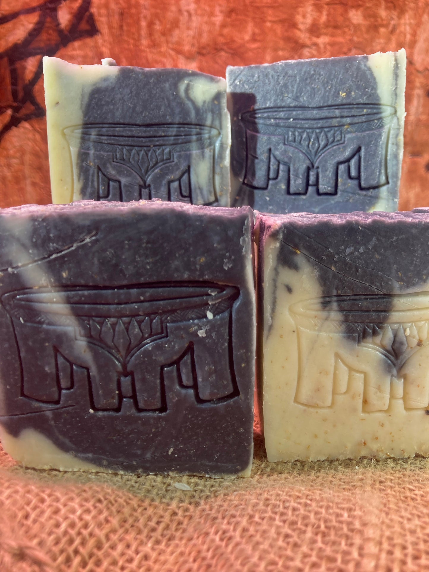 Four bars of soap with a brand logo embossed on them, placed on a textured surface.