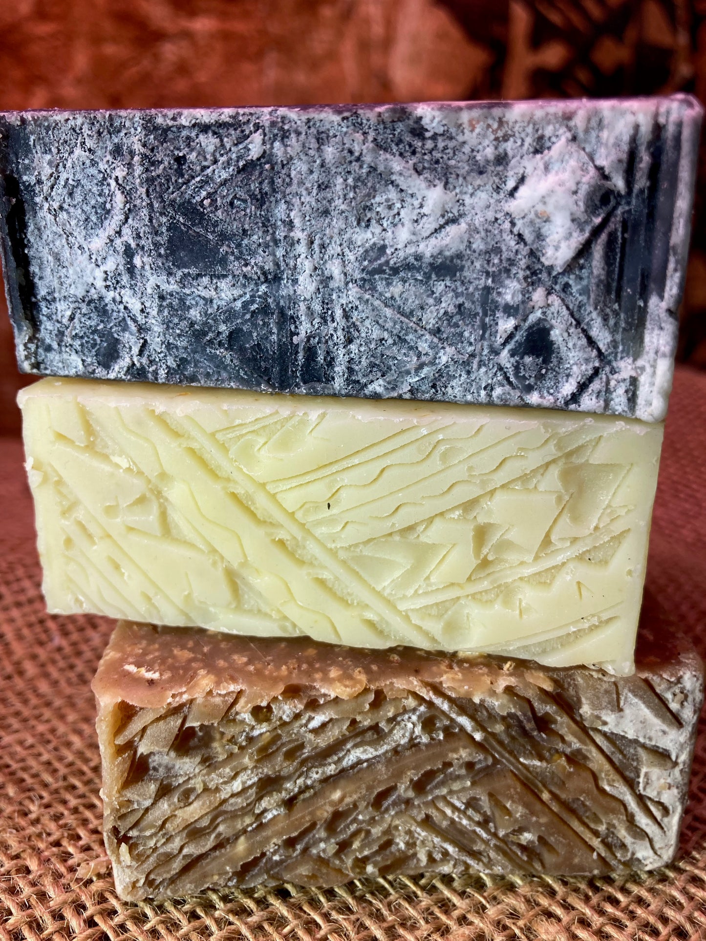 Three different colored soap bars stacked on a textured surface