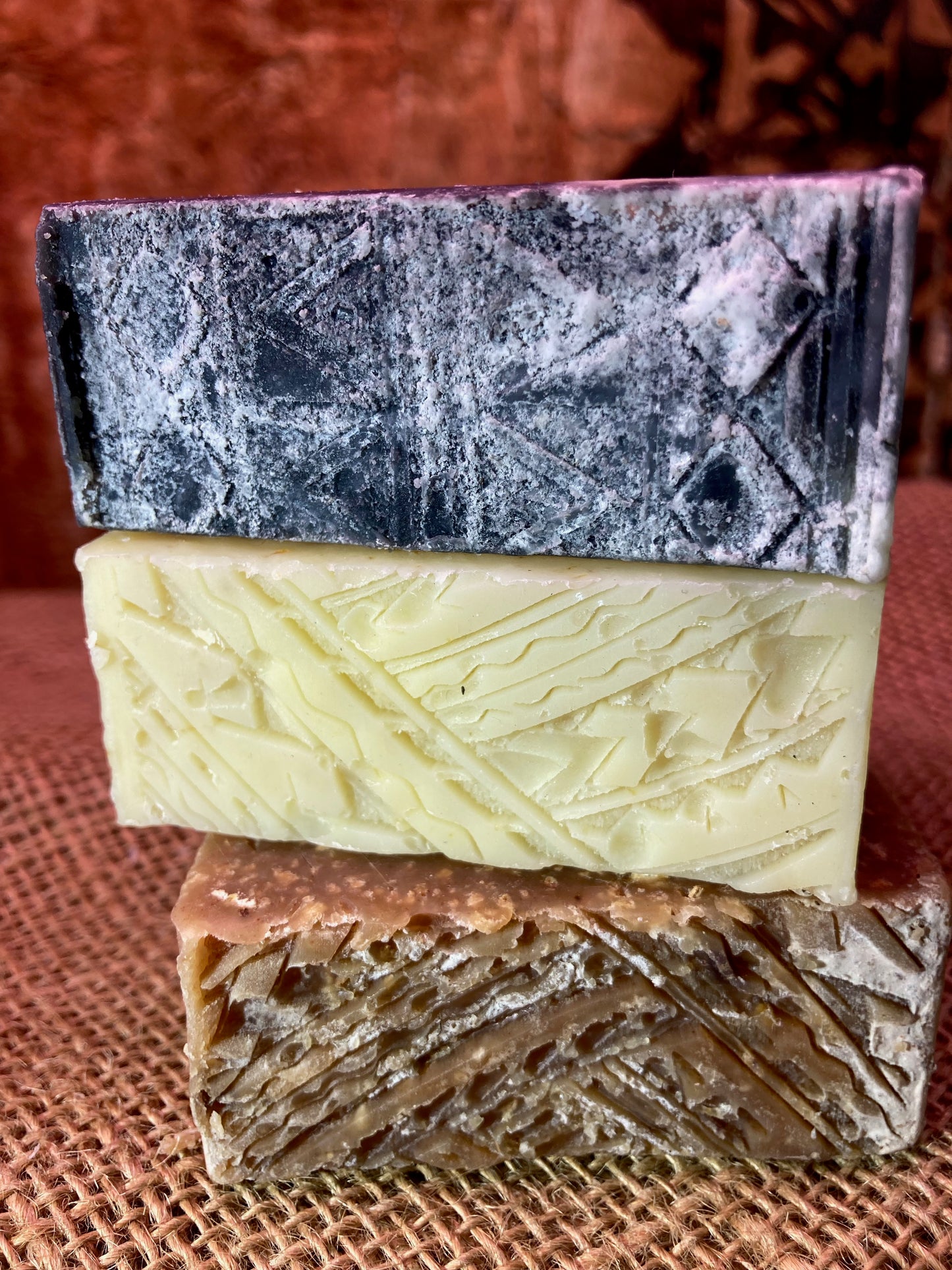 Three different colored soap bars stacked on a textured surface