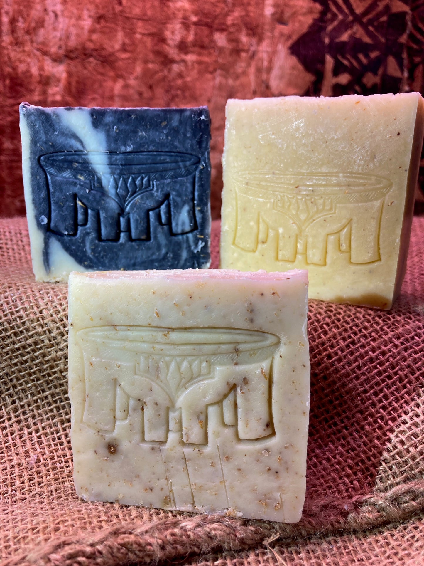 Three bars of soap with embossed designs on a textured fabric background