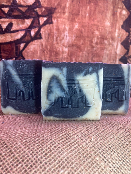 Three bars of black and white soap with embossed designs on a textured brown surface.