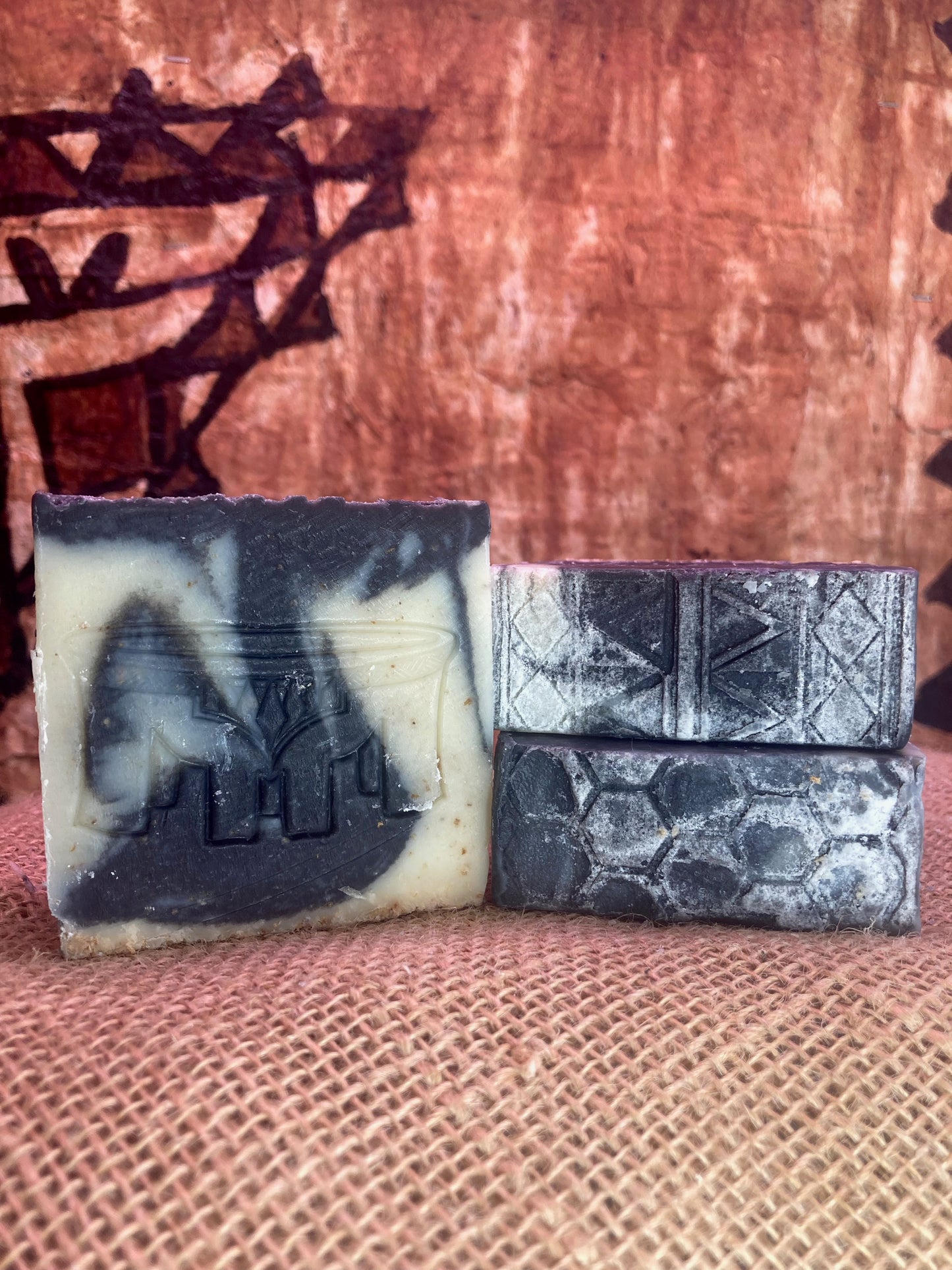 Three bars of soap with textured surfaces on a burlap bag with a tapa cloth tapestry in the background