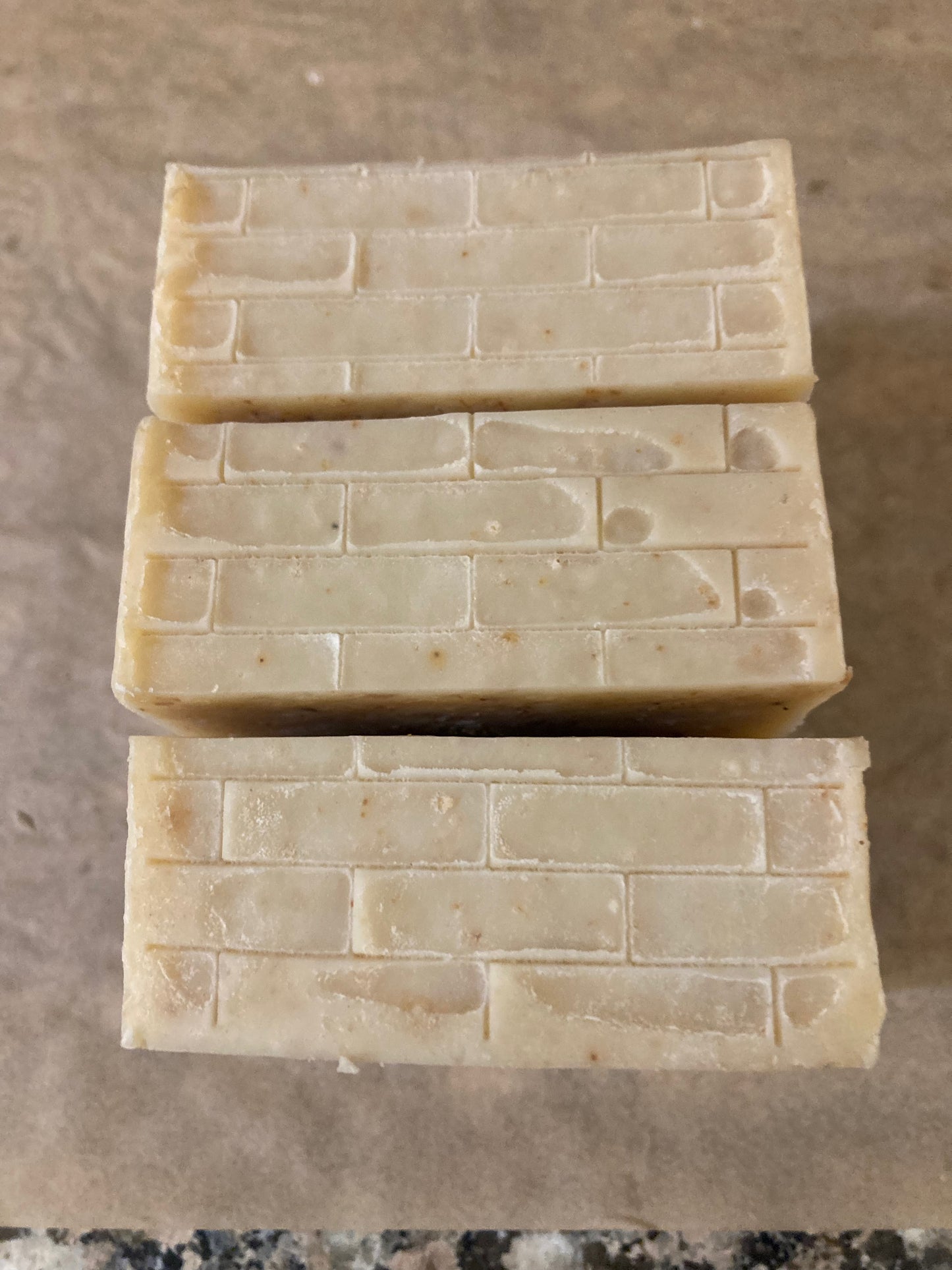 Three rectangular bars of soap stacked on a brown surface