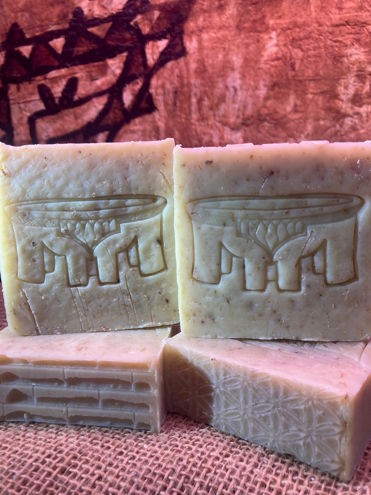 Two bars of soap with embossed designs standing on two bars of soap with textured designs on a burlap bag