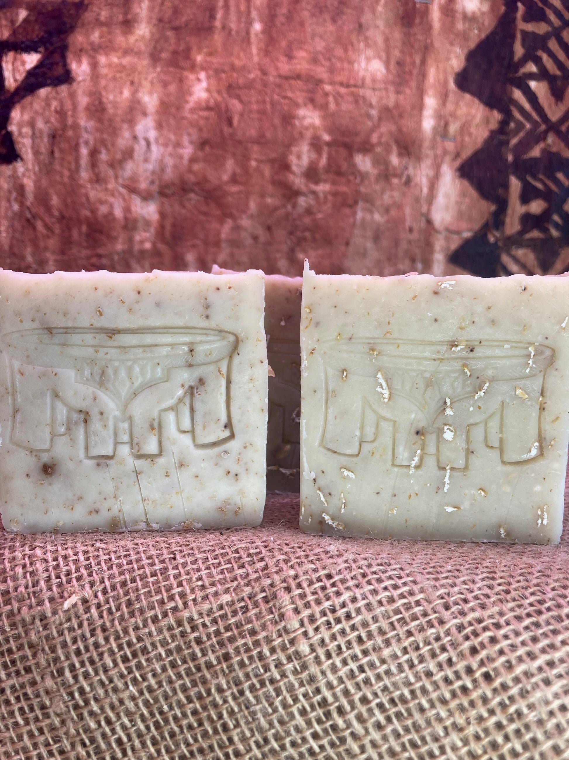 Two soap bars with embossed designs on a textured fabric background