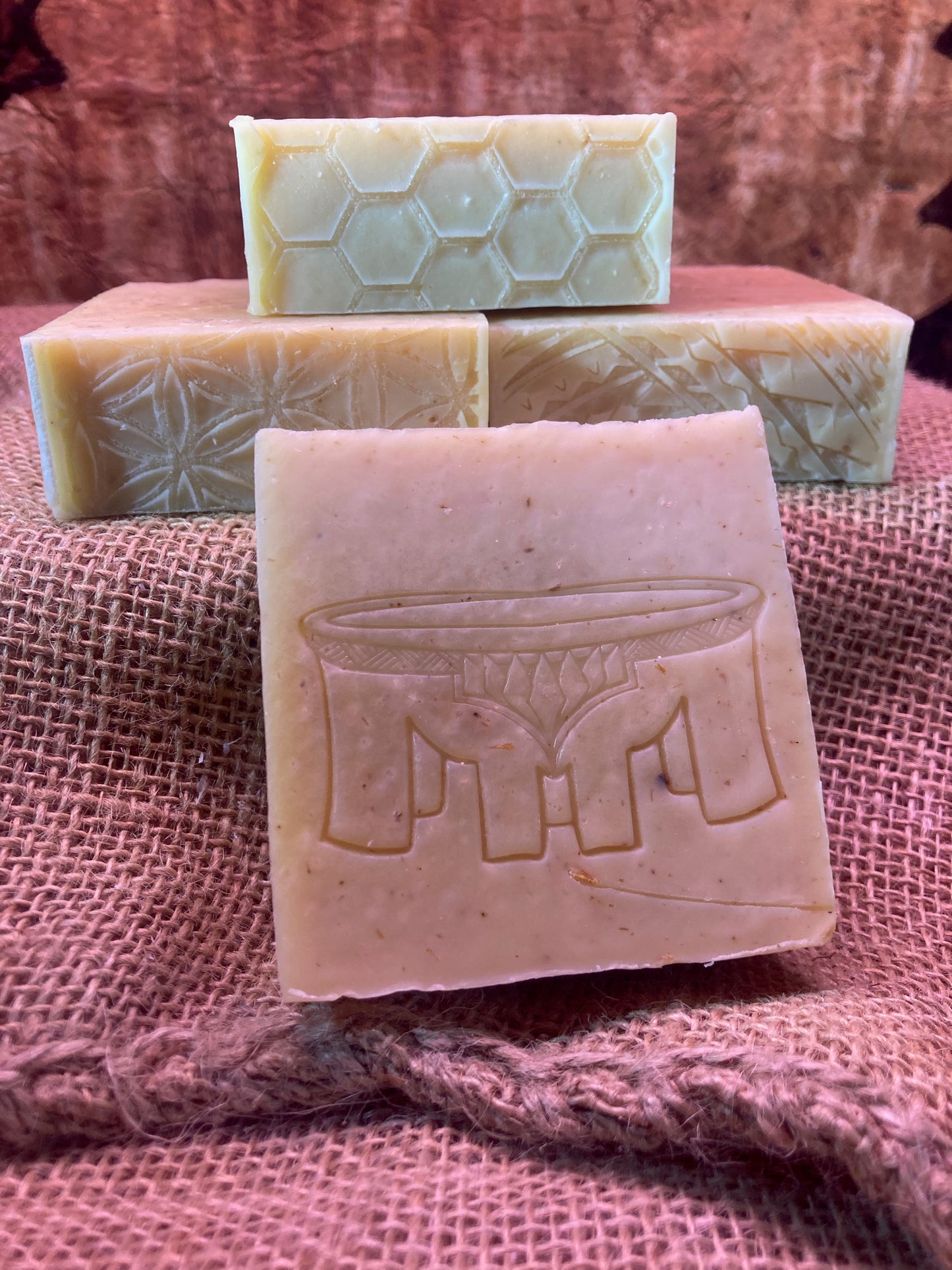 Four bars of soap with embossed designs on a pink textured fabric background