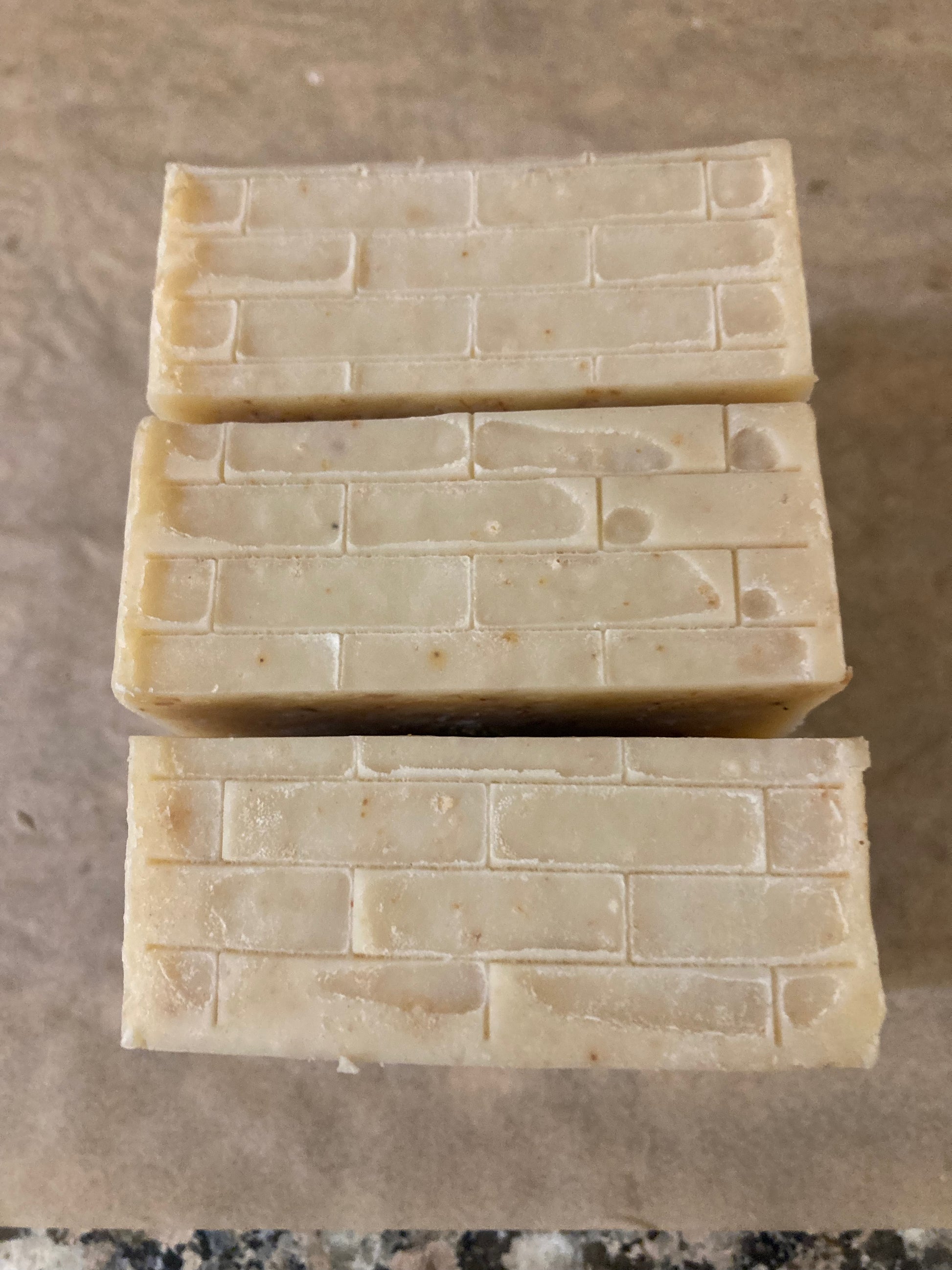 Three rectangular bars of soap stacked on a brown surface